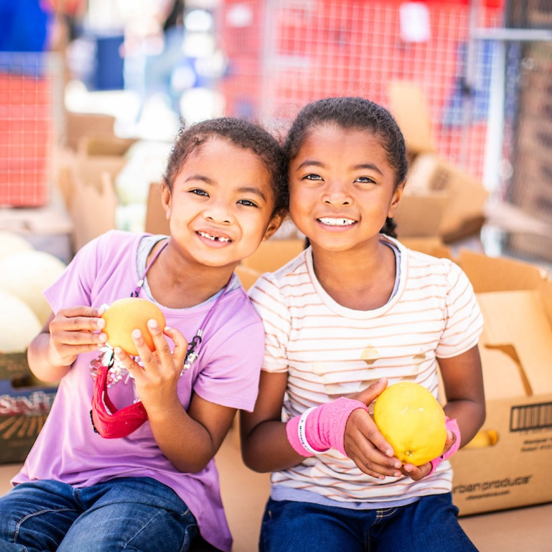 Two young girls holding fruit in a warehouse setting