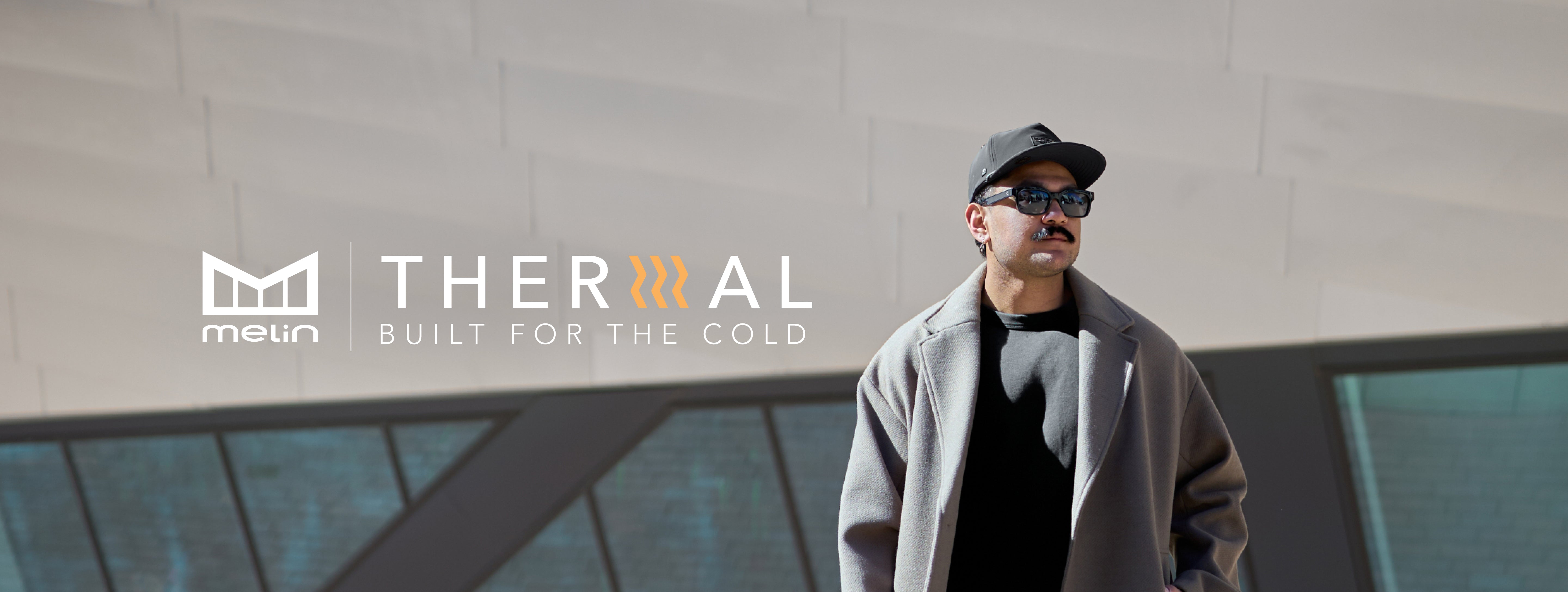 Man wearing a coat and sunglasses with 'melin THERMAL' branding in the background.