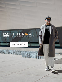 Person wearing a long coat and cap standing in front of a modern building with 'Melin Thermal' branding.
