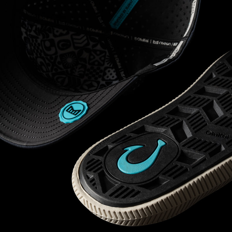Close-up of a the OluKai Ulele sandal with a blue logo on a dark background