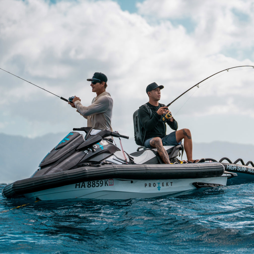 Two men wearing melin hats and OluKai sandals fishing on a jet ski in the ocean with a cloudy sky. 
