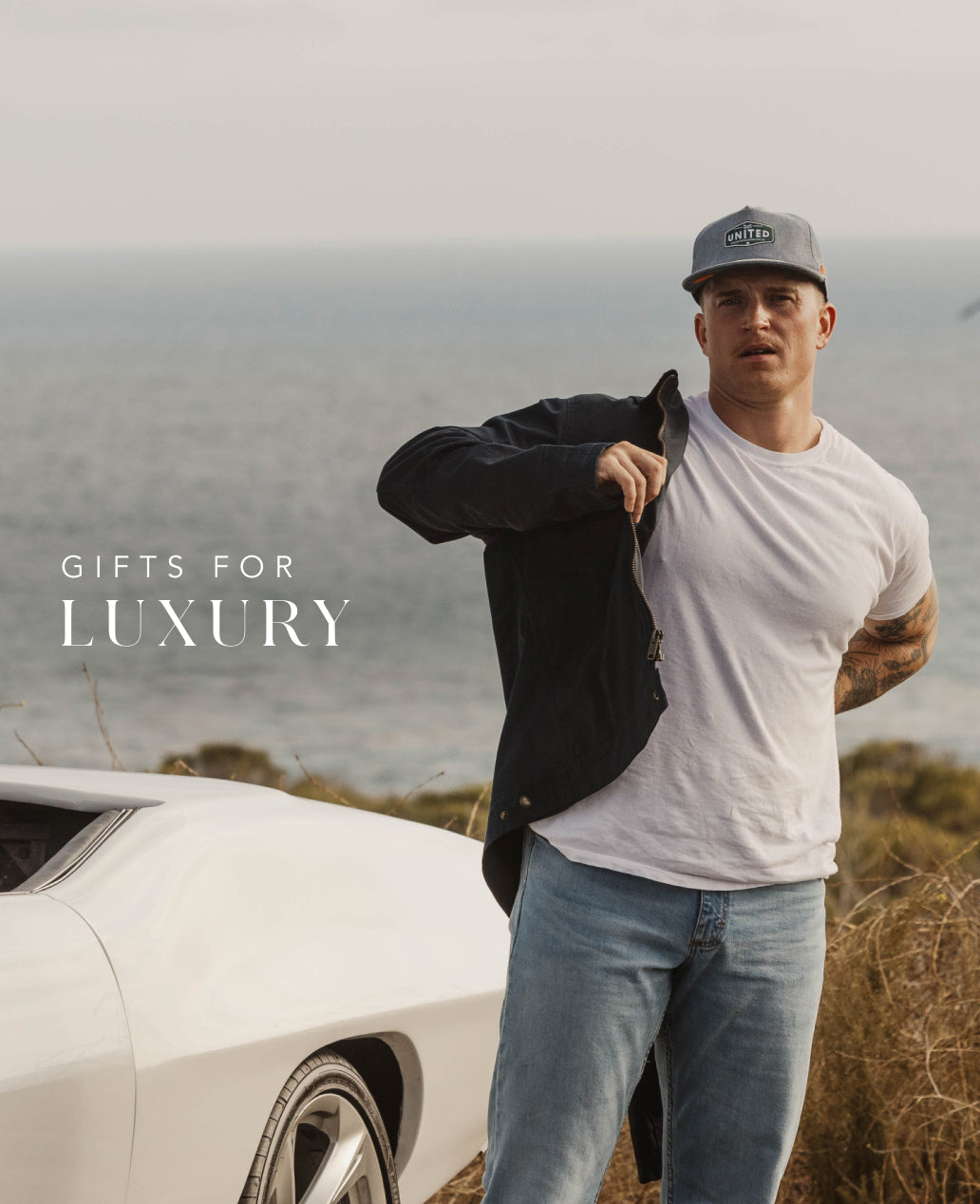 Man wearing the Coronado Mill United standing next to a white car with text 'Luxury Gifts' on a scenic background