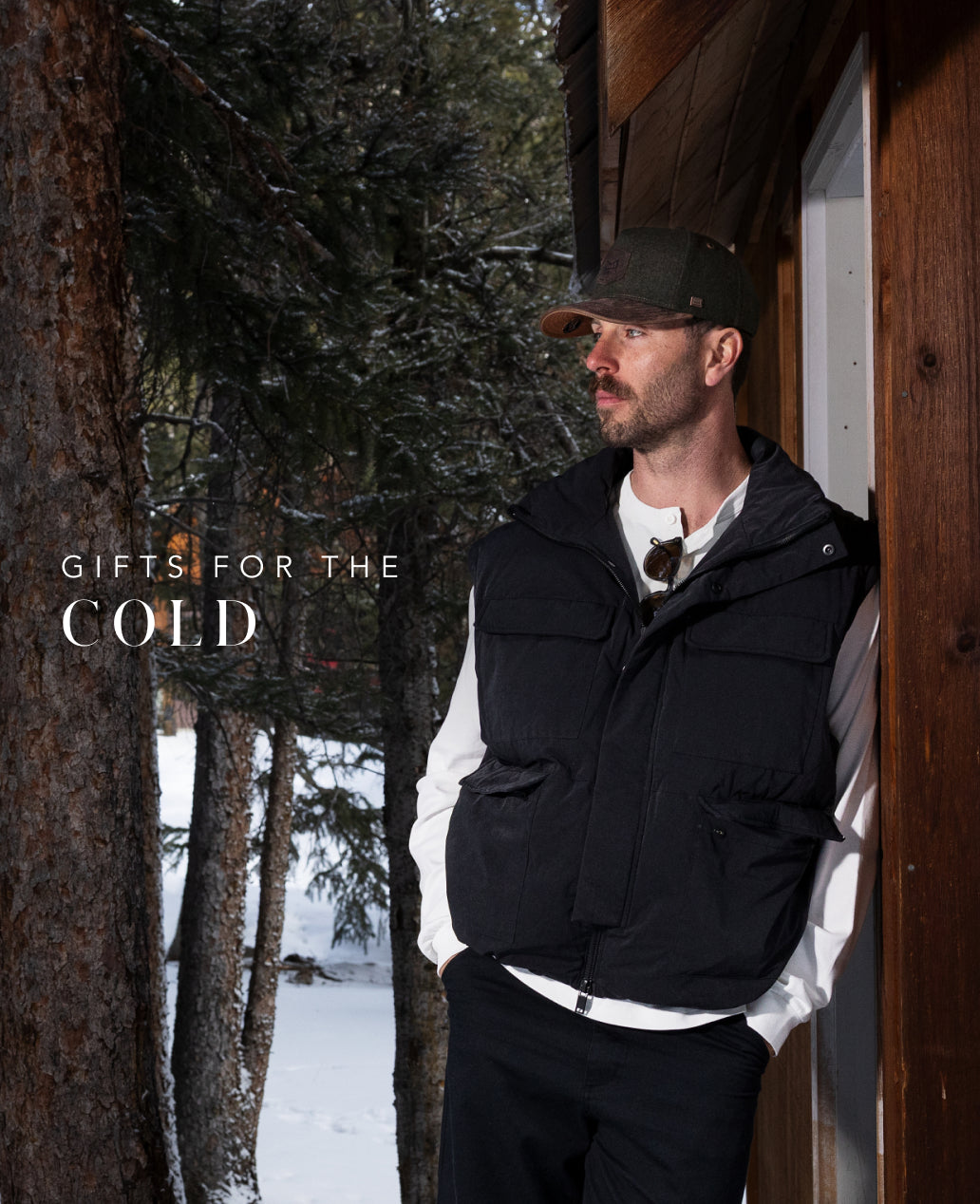 Man in a black vest wearing the Odysea Scout Thermal standing in a snowy forest with text 'Gifts for the Cold'.