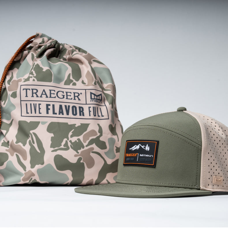 Camouflage bag and green melin cap with Traeger logo on a light gray background