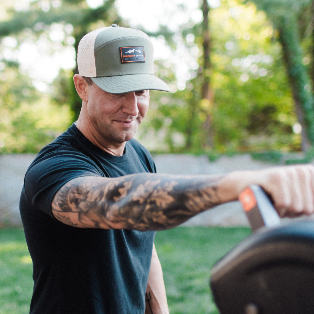 Alex Belew wearing the melin x Traeger hat while using a Traeger grill