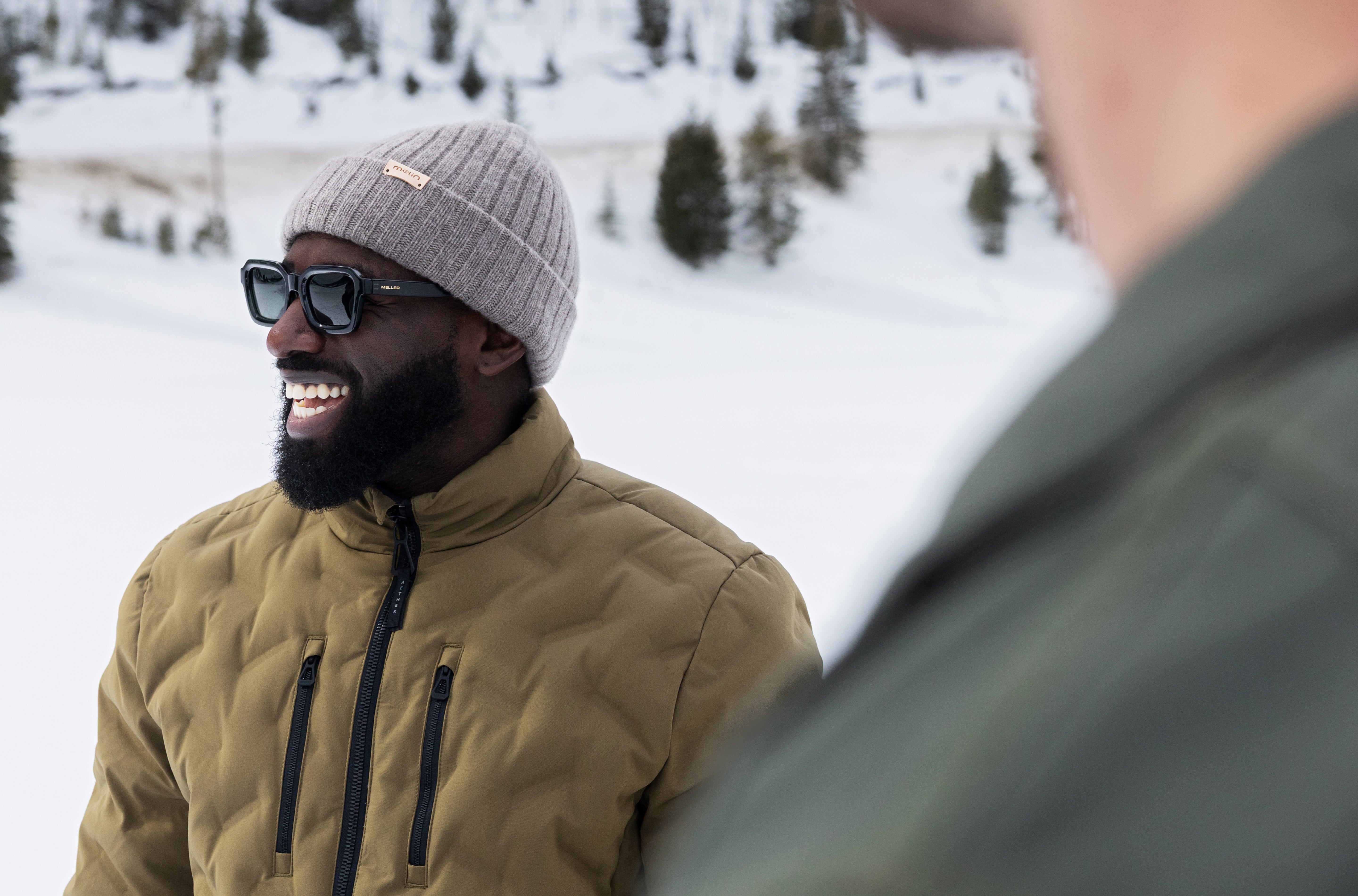 Person wearing a green jacket and melin All Day beanie in Heather Charcoal in a snowy landscape